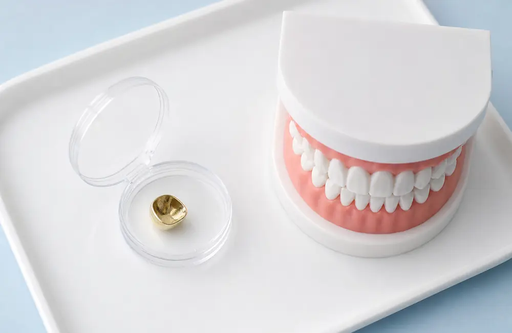 Loose gold cap in a small container beside a dental model